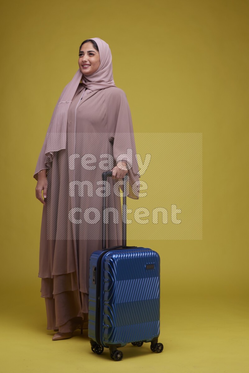 A woman With suit Case on a Yellow Background wearing Brown Abaya with Hijab
