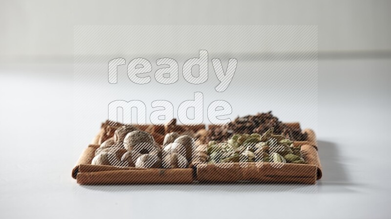 4 مربعات من أعواد القرفة ممتلئة بالهيل والقرفة والقرنفل وجوزة الطيب على أرضية بيضاء