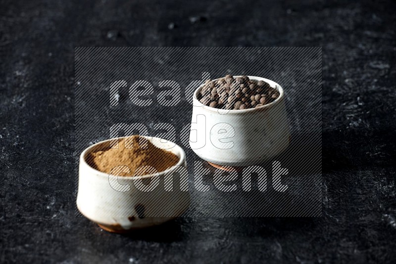 2 beige bowls, one full of allspice powder and the other full of whole balls on a textured black flooring