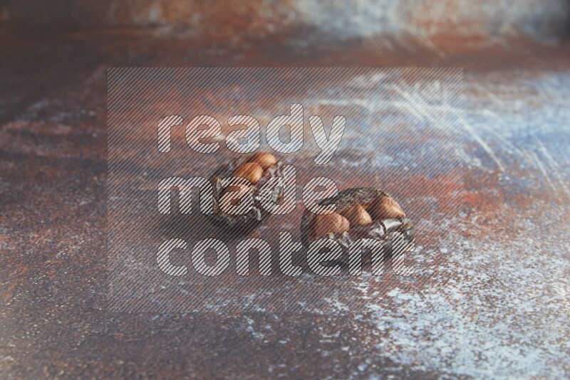 two hazelnut stuffed madjoul dates on a rustic reddish background
