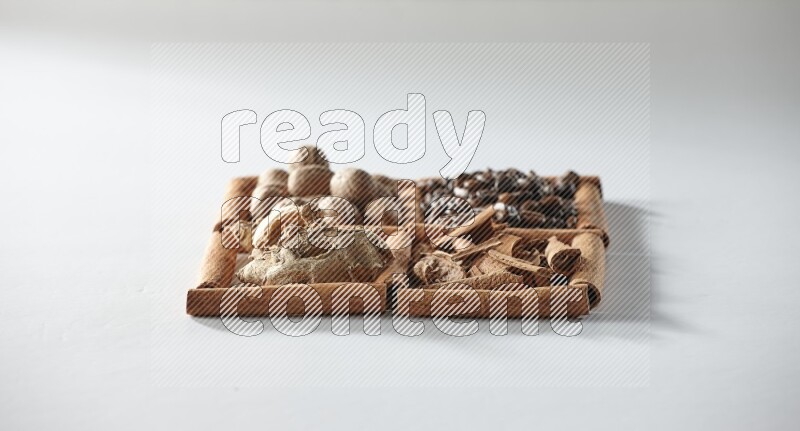 4 مربعات من أعواد القرفة ممتلئة بحبوب القهوة وجوزة الطيب والقرفة والزنجبيل المجفف على أرضية بيضاء