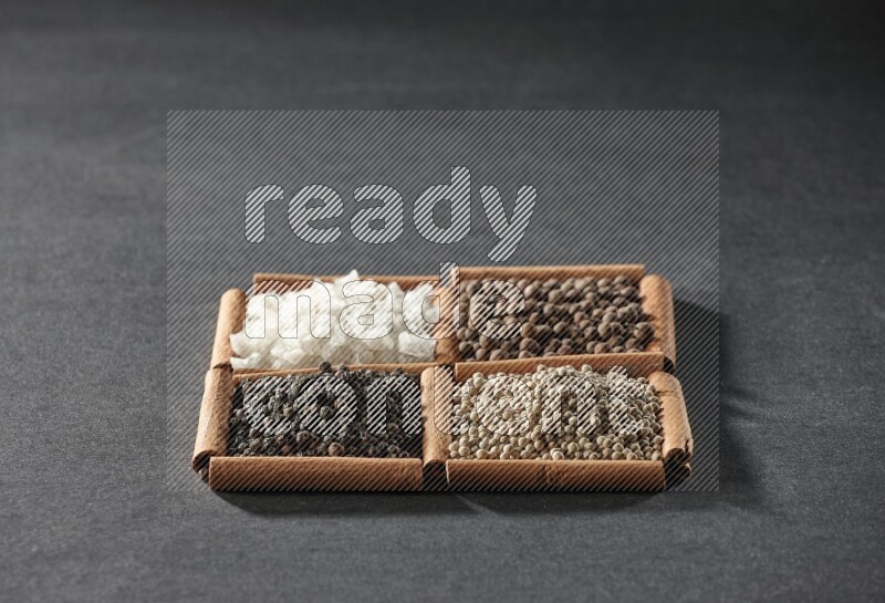 4 مربعات من عيدان القرفة ممتلئة بحبوب الفلفل الأسود والفلفل الأبيض وبهار الفلفل الحلو والملح الأبيض على أرضية سوداء