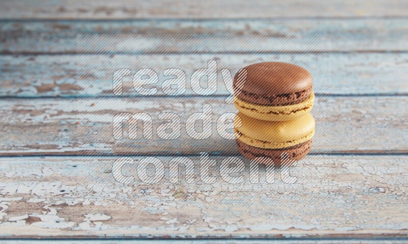 45º Shot of two Yellow and Brown Chai Latte macarons on light blue wooden background