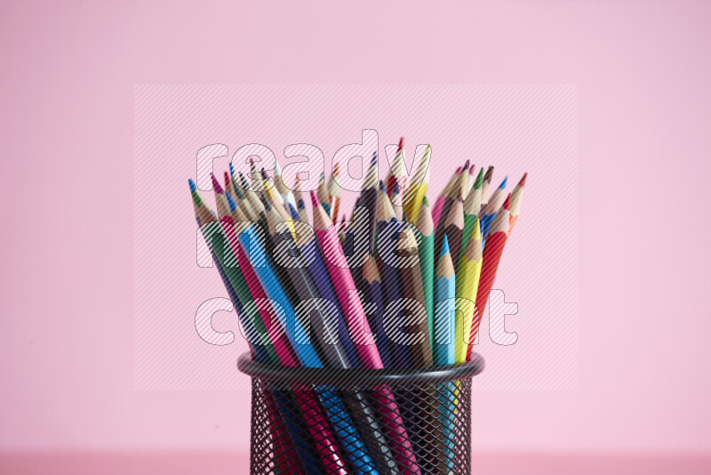 Pens, pencils and other different school supplies in a metal pen holder on rose background