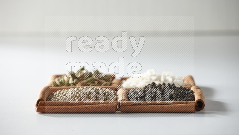 4 squares of cinnamon sticks full of cardamom, salt, white pepper and black pepper on white flooring