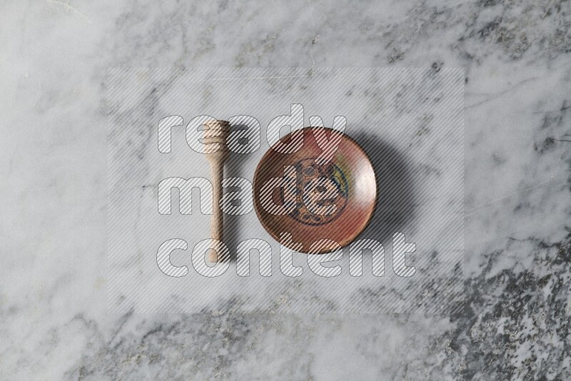 Decorative pottery plate with wooden honey dipper on the side on grey marble background