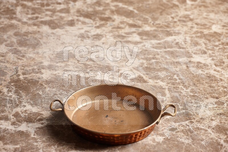 A small copper pan on beige marble background