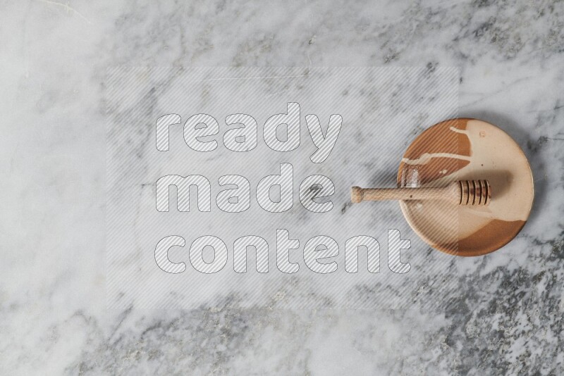 Multicolored pottery plate with wooden honey dipper in it on grey marble background
