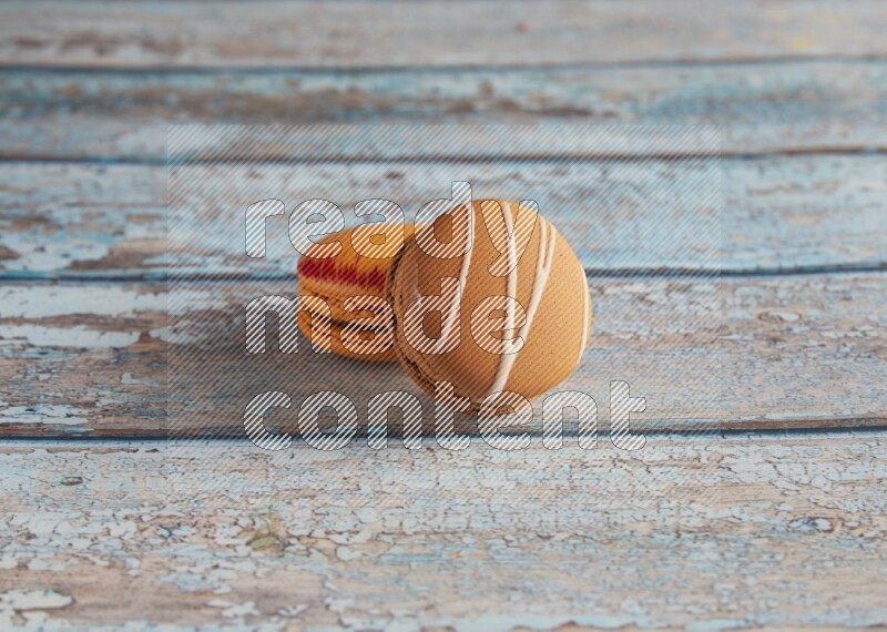 45º Shot of of two assorted Brown Irish Cream, and Orange Exotic macarons on light blue background