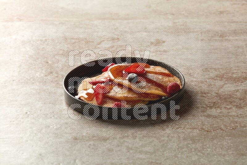 Three stacked mixed berries pancakes in a black plate on beige background