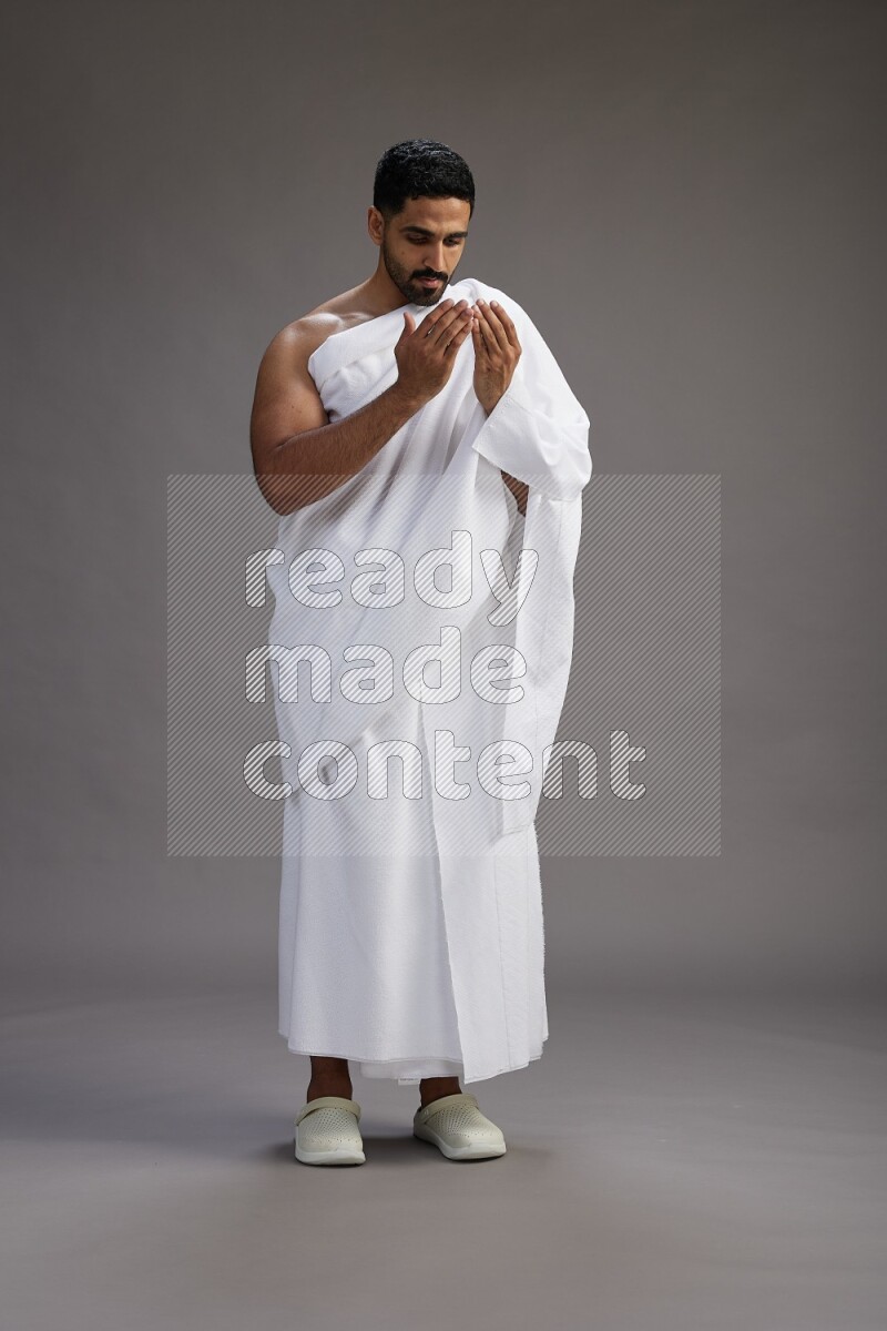 A man wearing Ehram Standing performing dua'a on gray background