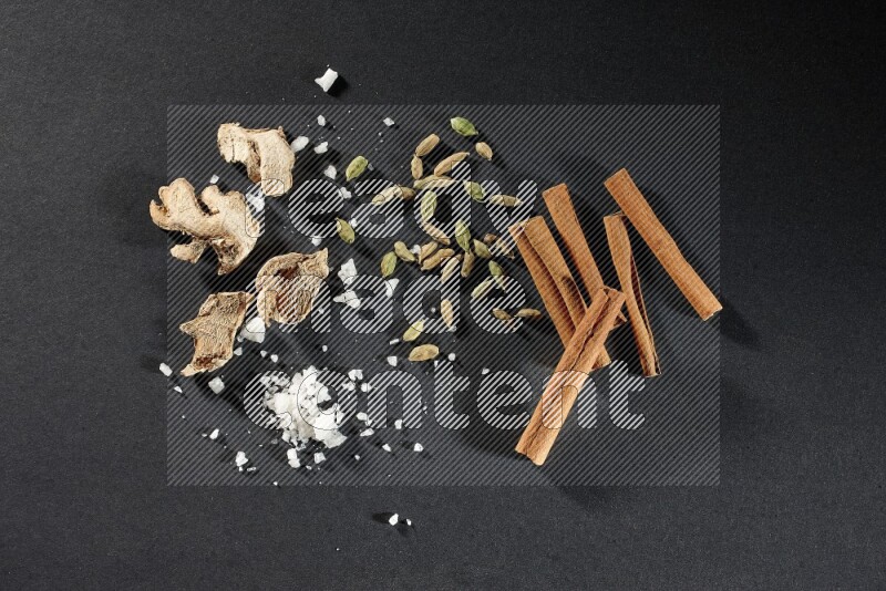 Ginger, salt, cardamom and cinnamon sticks on black flooring