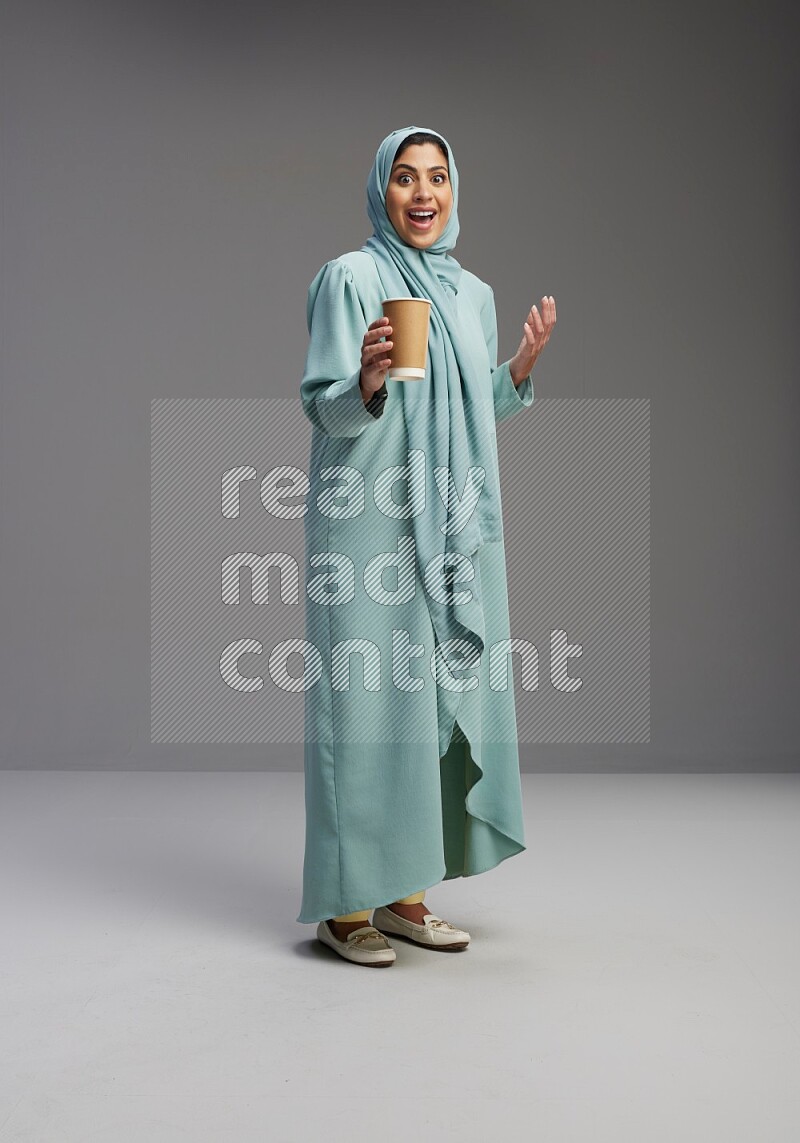Saudi Woman wearing Abaya standing  holding paper cup on Gray background