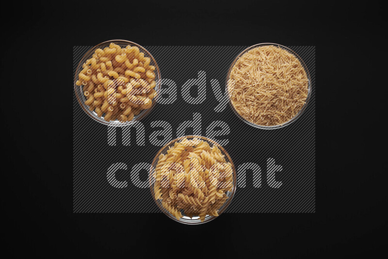 Different pasta types in glass bowls on black background