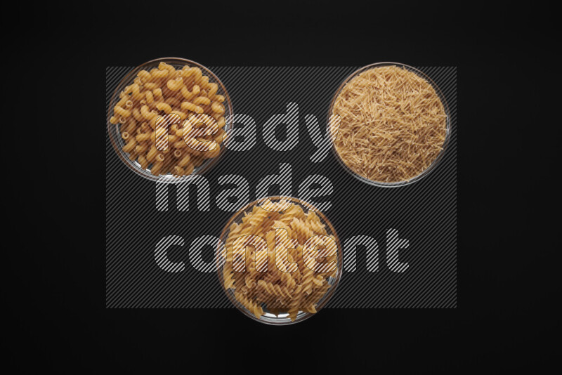 Different pasta types in glass bowls on black background