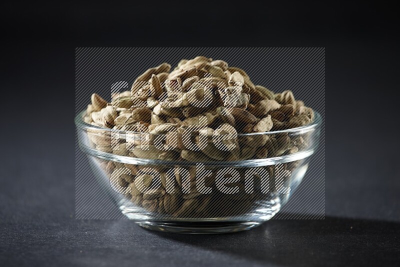 A glass bowl full of cardamom on black flooring