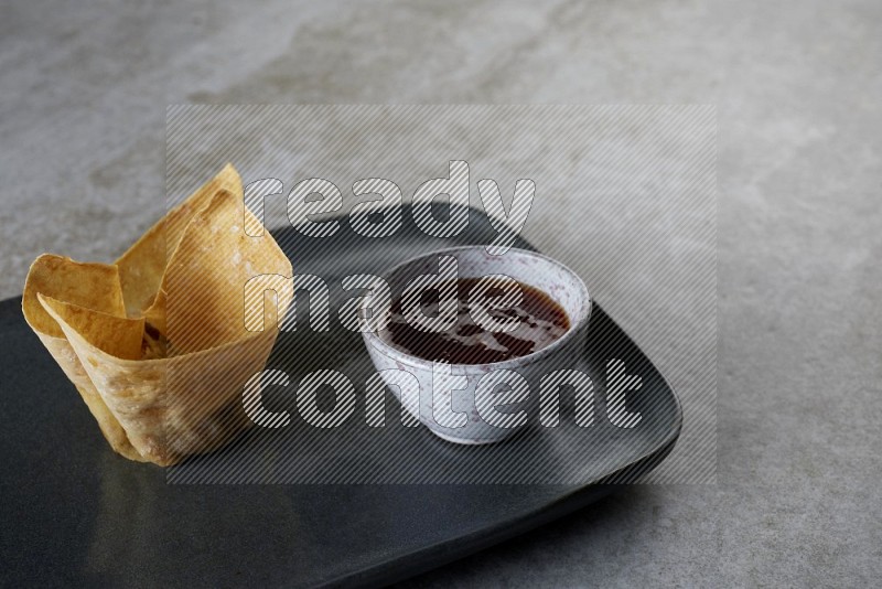 wonton cups with soy sauce ramkin on rectangle dark grey ceramic plate on grey textured counter top