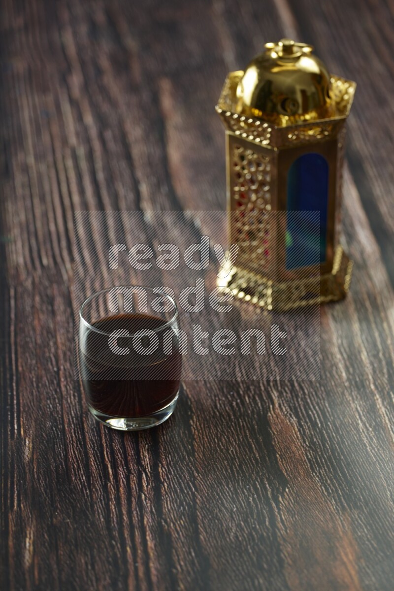 A golden lantern with different drinks, dates, nuts, prayer beads and quran on brown wooden background