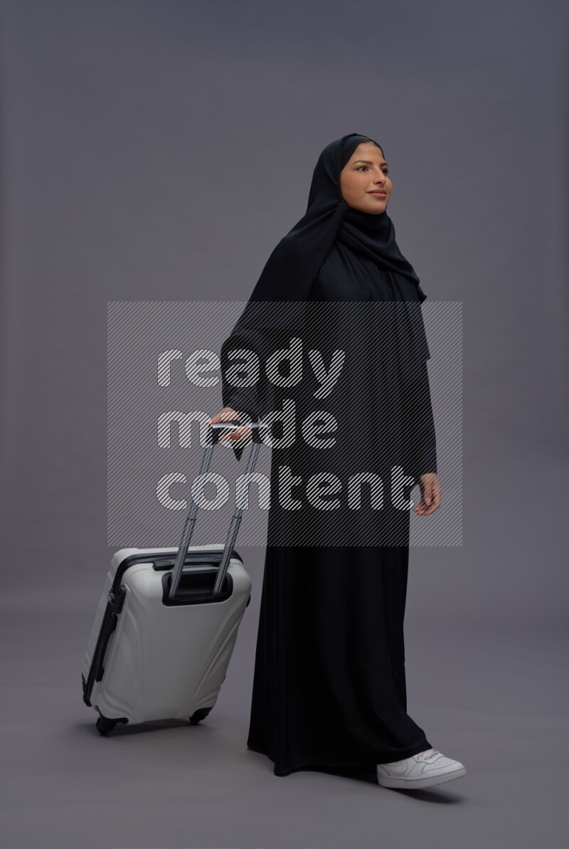 Saudi woman wearing Abaya standing holding bag on gray background