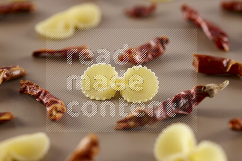 Raw pasta with different ingredients such as cherry tomatoes, garlic, onions, red chilis, black pepper, white pepper, bay laurel leaves, rosemary and cardamom on beige background