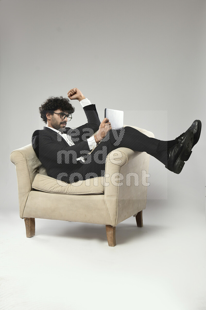 A man wearing formal sitting on a chair gaming on a tablet on white background
