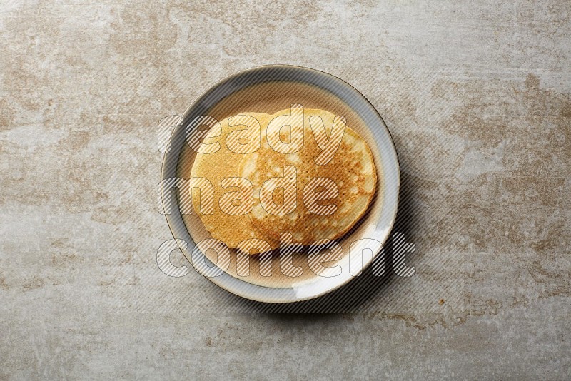 Two stacked plain pancakes in a bicolor plate on beige background