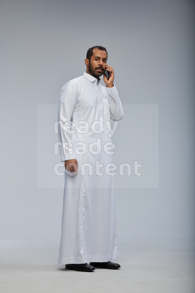 Saudi man wearing Thob standing talking on phone on Gray background