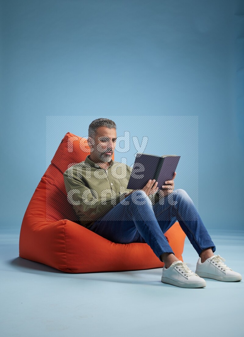A man sitting on an orange beanbag and reading a book