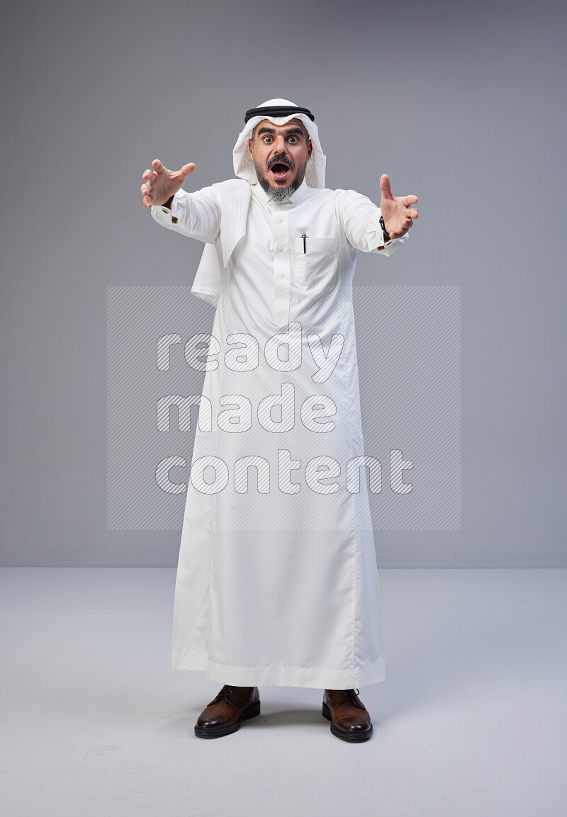 Saudi man Wearing Thob and white Shomag standing interacting with the camera on Gray background