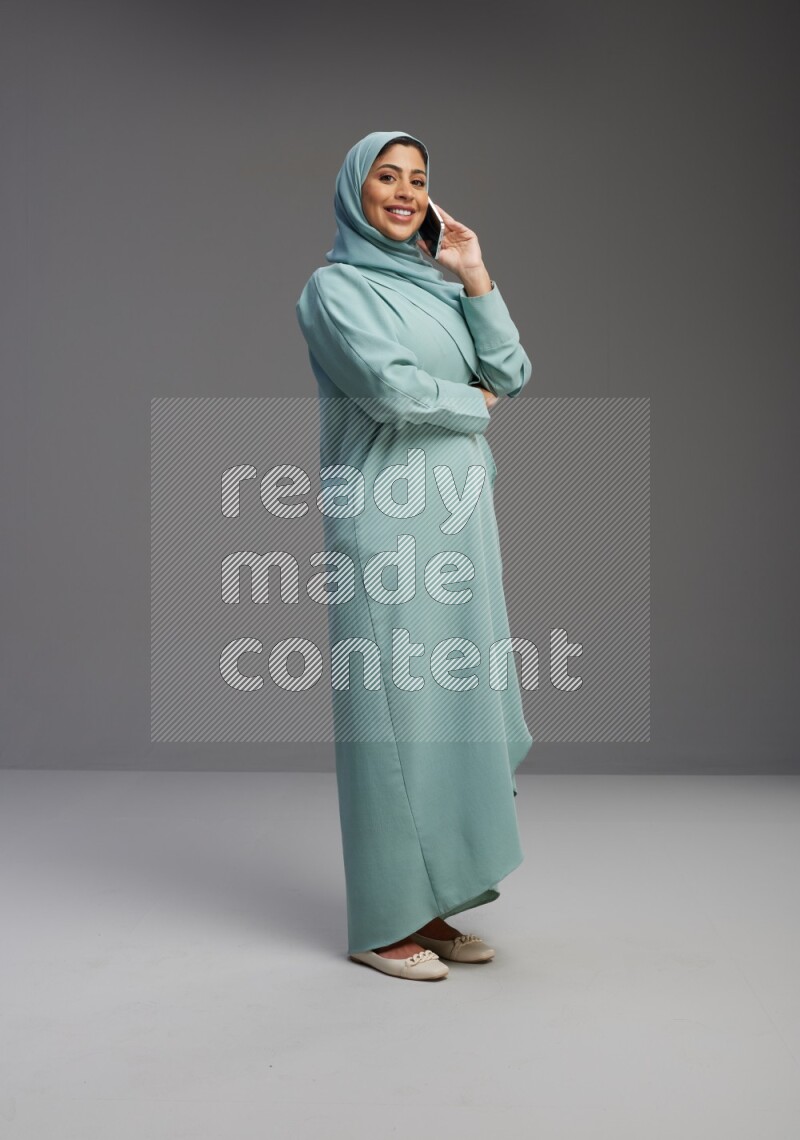 Saudi Woman wearing Abaya standing talking on phone on Gray background