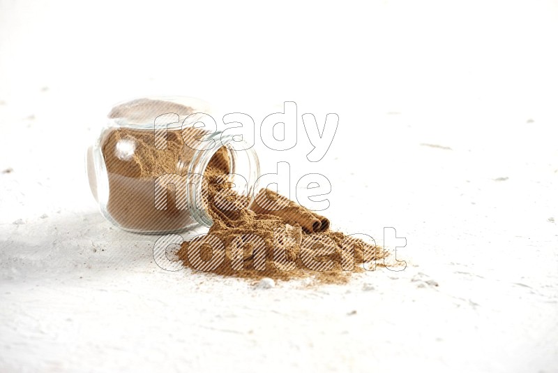 Flipped glass jar full of cinnamon powder with some pieces of cinnamon sticks on a textured white background