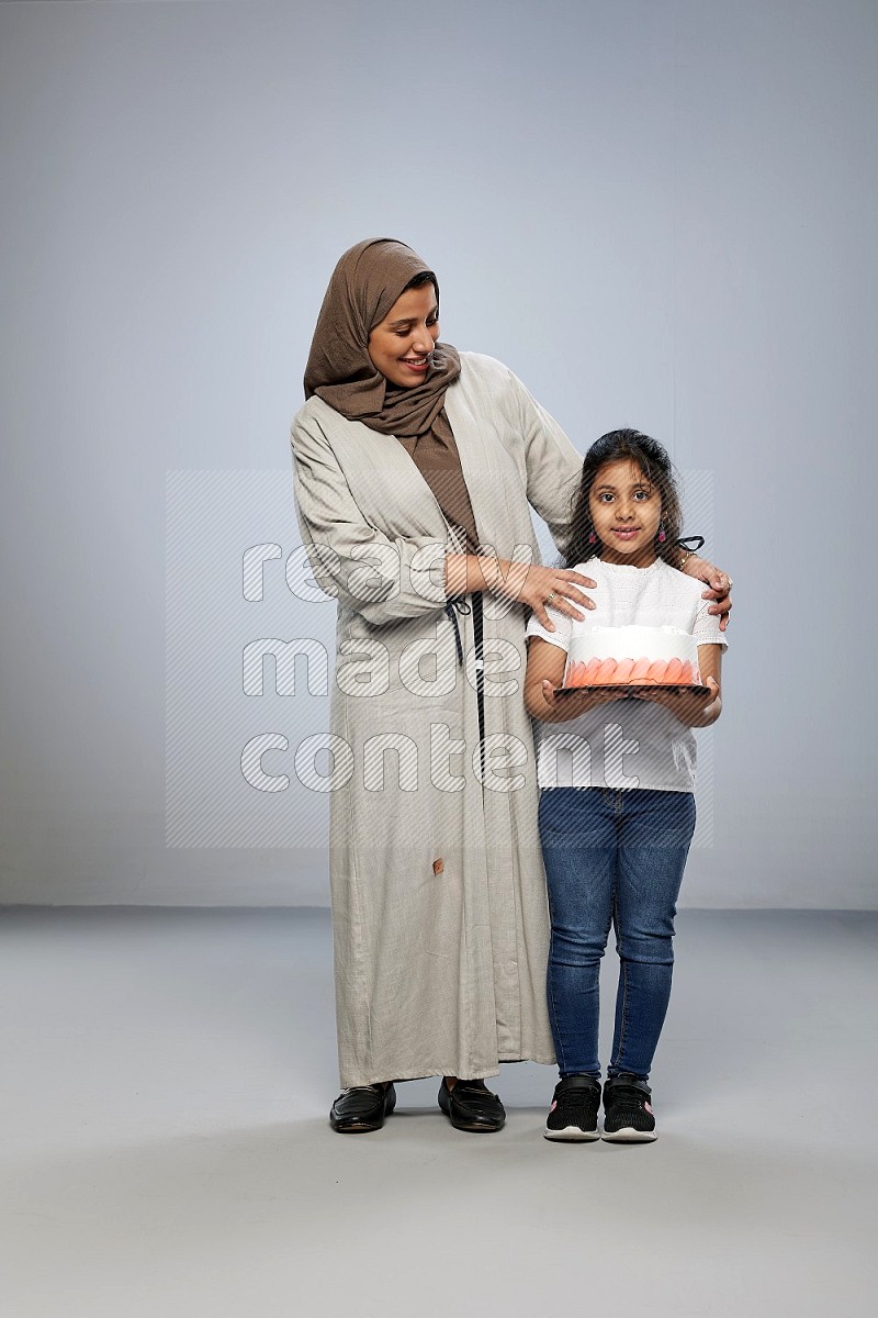 A girl giving a cake to her mother on gray background