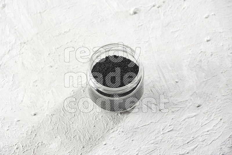 A glass jar full of black seeds on a textured white flooring