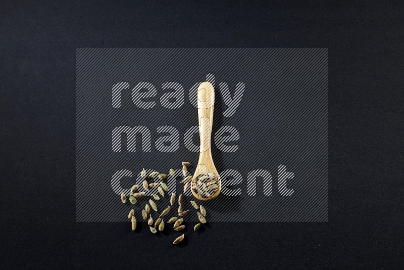 A wooden spoon full of cardamom on black flooring