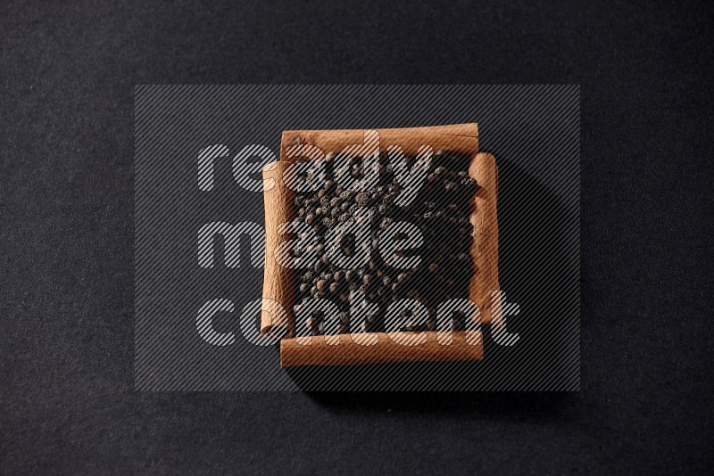 A single square of cinnamon sticks full of black pepper on black flooring