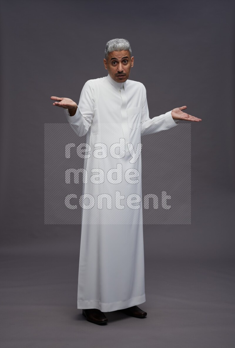 Saudi man wearing thob standing interacting with the camera on gray background