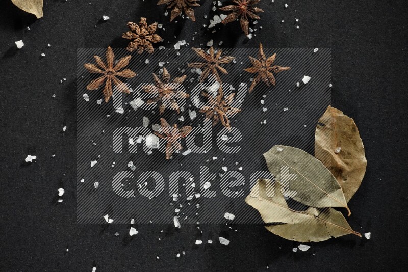 Salt, star anise and bay laurel on black flooring