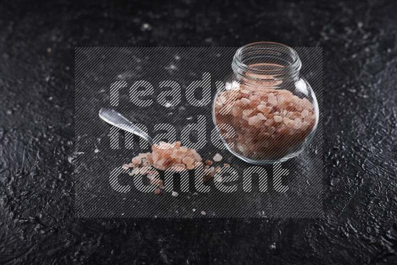 A glass jar full of coarse himalayan salt crystals on black background