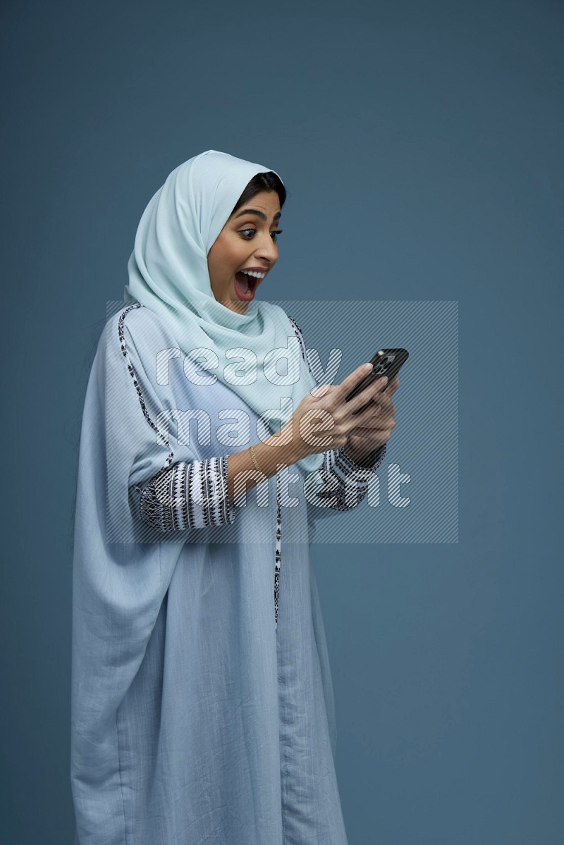 A Saudi woman Texting in a blue background wearing a blue Abaya with hijab