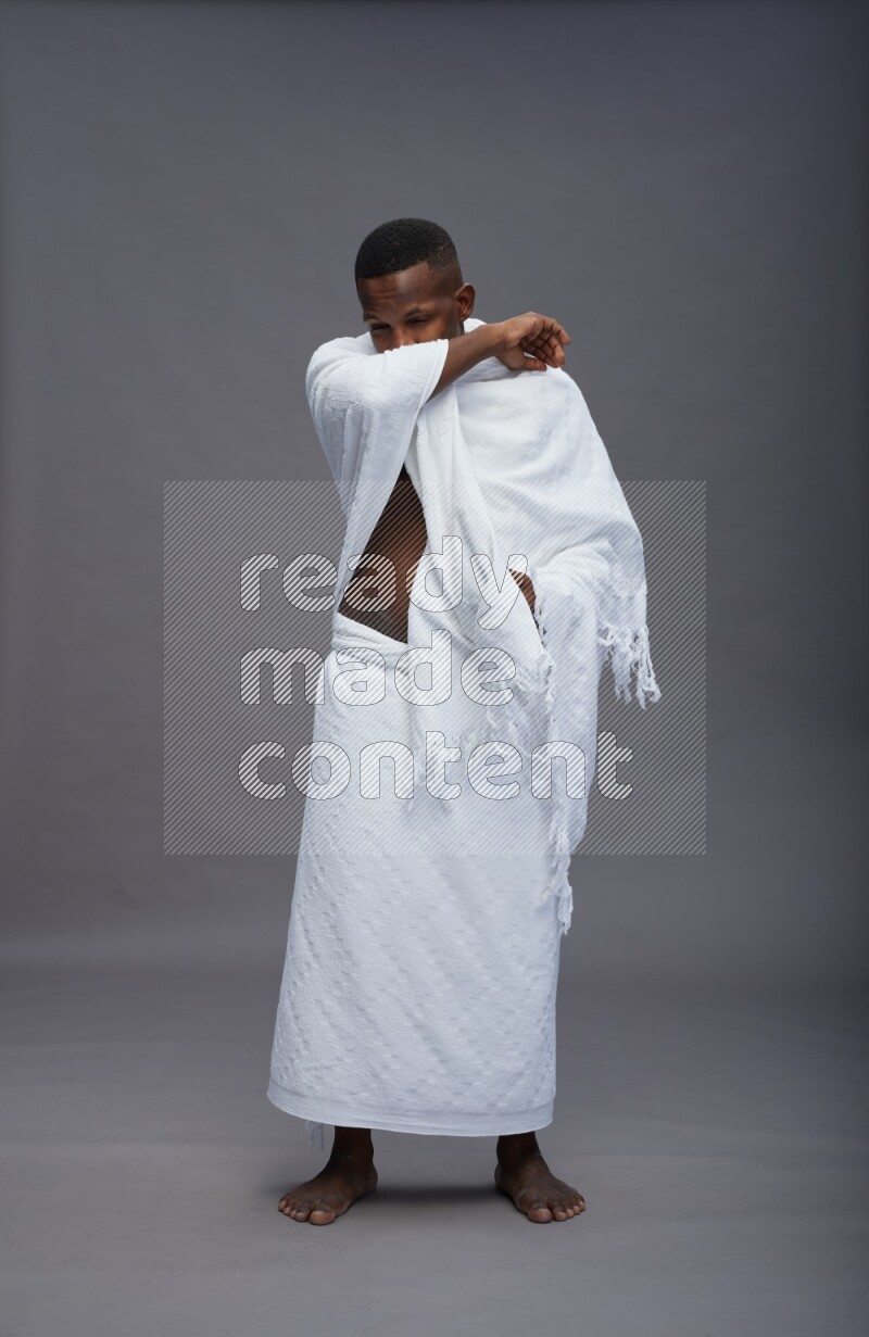 A man wearing Ehram standing showing how to sneeze on gray background