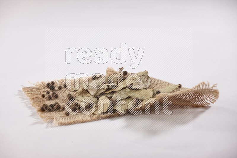 Dried bay leaves and allspice berries on a piece of burlap on white flooring in different angles