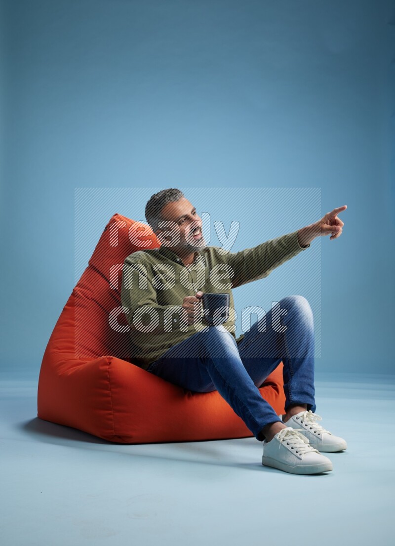 A man sitting on an orange beanbag and drinking coffee