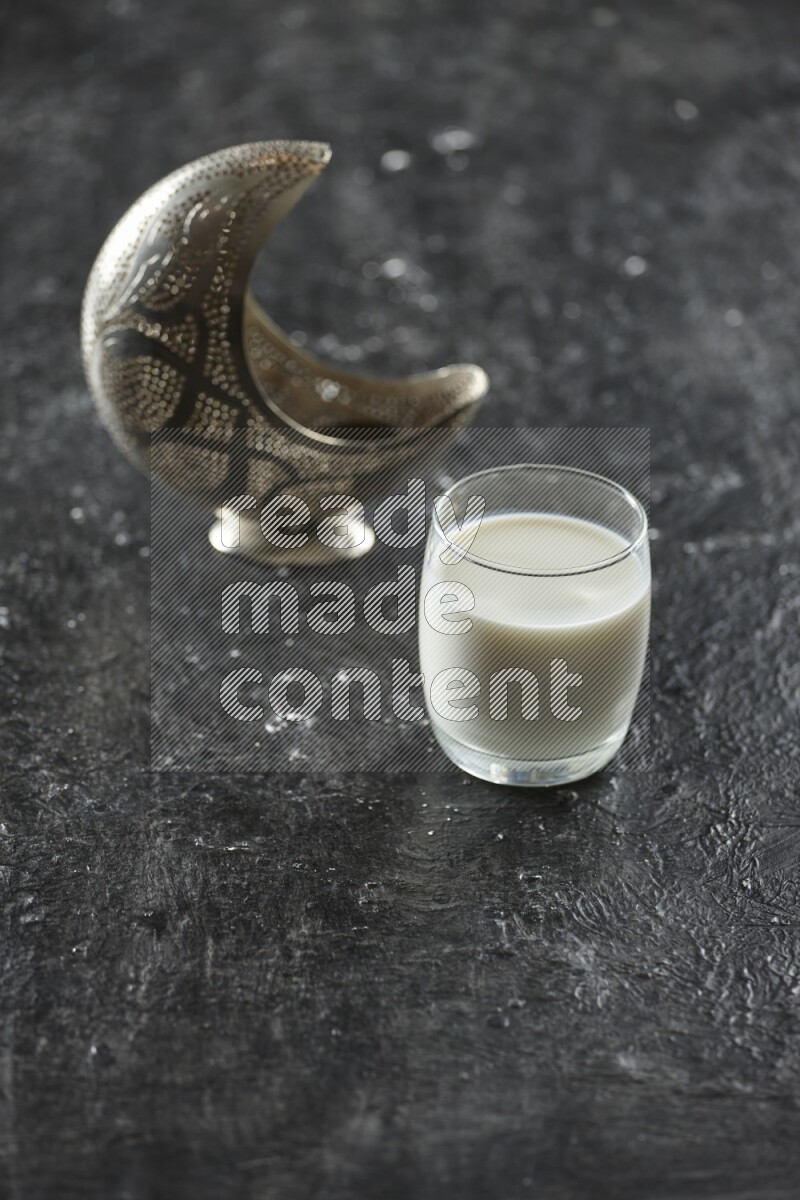 A silver lantern with different drinks, dates, nuts, prayer beads and quran on textured black background