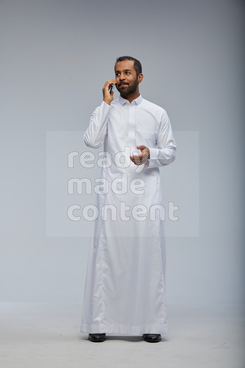Saudi man wearing Thob standing talking on phone on Gray background