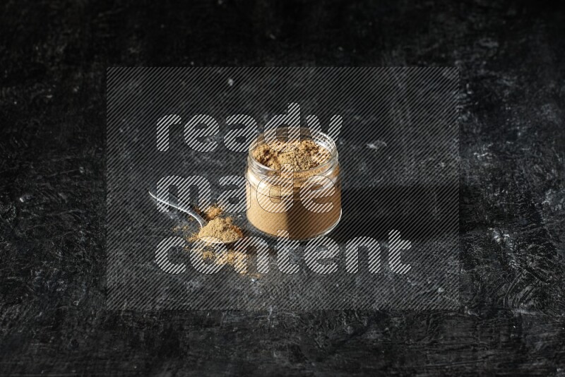 وعاء زجاجي للتوابل وملعقة معدنية ممتلئان ببودرة بهار الفلفل الحلو على خلفية سوداء