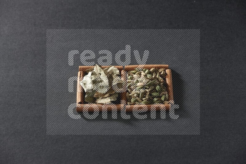 مربعان من أعواد القرفة ممتلئان بحبوب الهيل وأوراق الغار علي خلفية سوداء