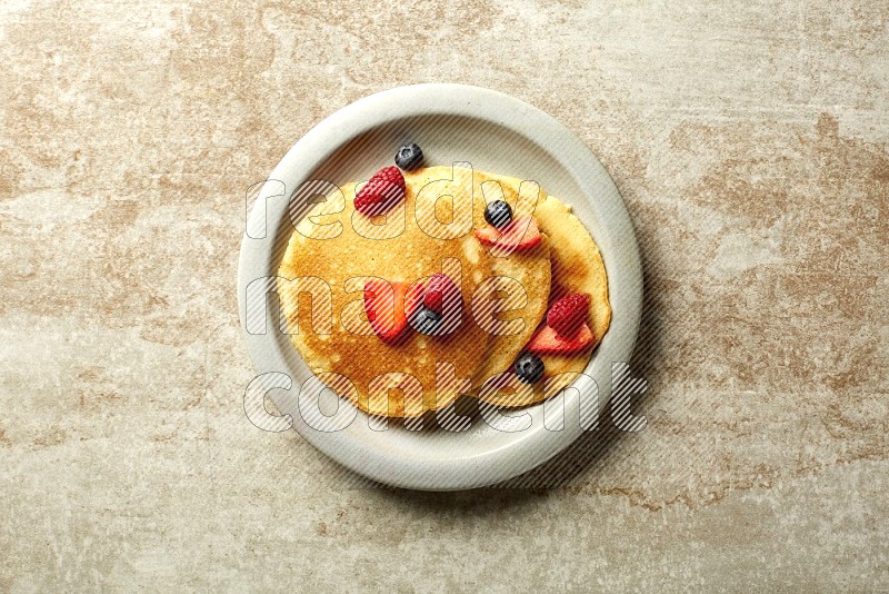 Three stacked mixed berries pancakes in a grey plate on beige background