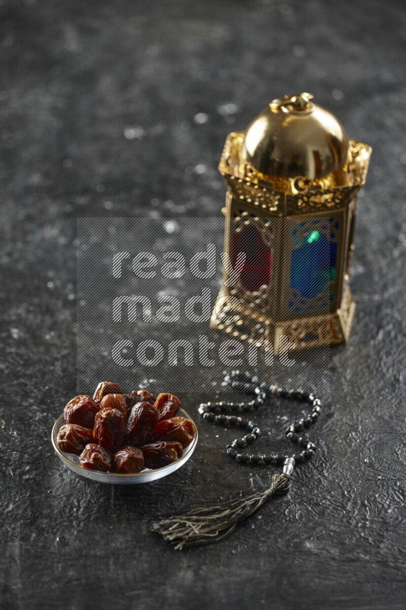 A golden lantern with different drinks, dates, nuts, prayer beads and quran on textured black background