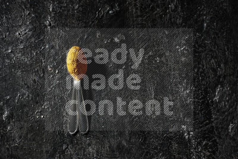 ملعقتان معدنيتان ممتلئتان ببودرة الكركم على خلفية سوداء