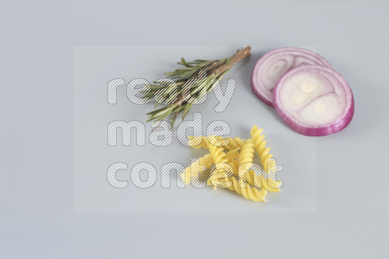 Raw pasta with different ingredients such as cherry tomatoes, garlic, onions, red chilis, black pepper, white pepper, bay laurel leaves, rosemary, cardamom and mushrooms on light blue background